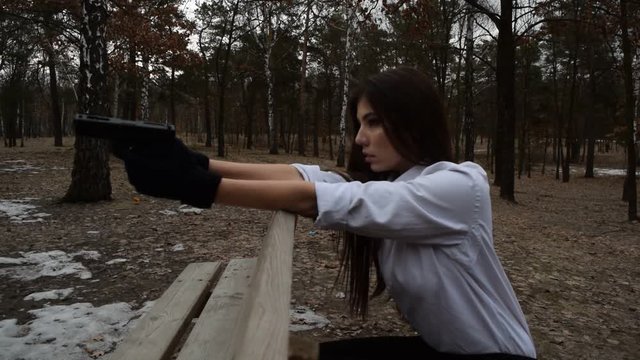 Young brunette girl shoots with gun in dark forest.