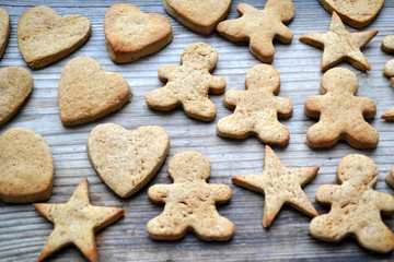 Gingerbread cookies in shapes of heart, star and man with cinnamon stick and ginger root on wooden table