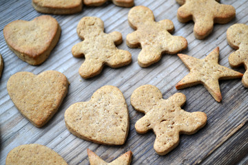 Gingerbread cookies in shapes of heart, star and man with cinnamon stick and ginger root on wooden table