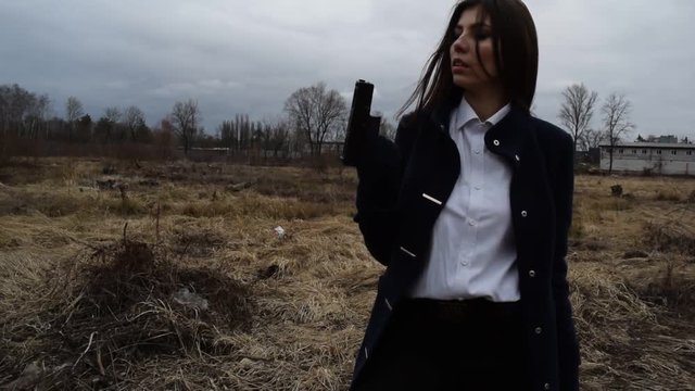 Young brunette girl shoots with a gun in a coat on the field.