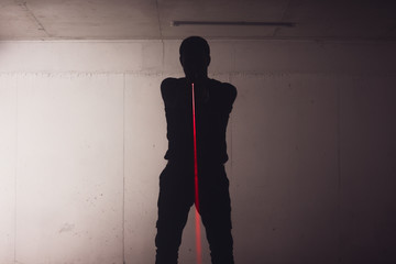 Silhouette of an armed man holding his gun and pointing with his laser beam at a target.