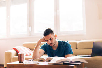Handsome student studying with few opened books next to him.