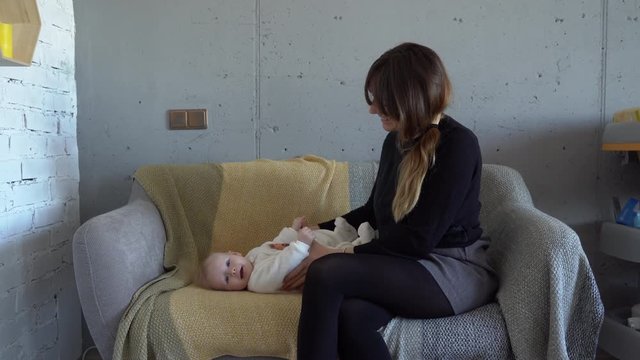 A young beautiful mother plays with her five months baby on a sofa in the living room