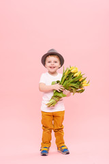 Adorable smiling child with spring flower bouquet looking at camera isolated on pink. Little...