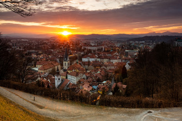 Fototapeta na wymiar Sunset in Ljubljana on the last days of winter. A view, from the castle hill towards Trnovo, of the setting sun over the hills on the west and under the clouds.