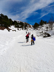 group of excursionists walking on snowshoes and stick poles on the white snow of the winter on a path of a snowy mountain in a clear sunny day