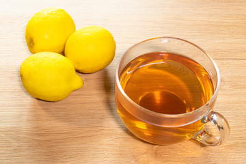 Top view of a cup of tea. A cup is on the table. Near the cup are three fresh lemons. Table light color. Sunny morning or afternoon. Home comfort and good atmosphere.