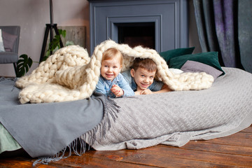 happy cute brother 6 years old and sister 3 years old in a cozy home environment on the bed playing, kissing and hugging, happy family relationships