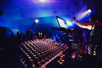 Sound equipment in nightclub party. DJ console, people dancing in background, around bright lights