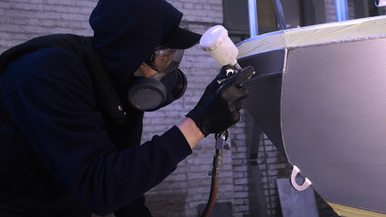 A professional guy (man) in the garage covers the yacht (transport) with a mini-jet (sprays) by applying paint (ceramics) to the surface using a protective suit dispenser and protective glasses.