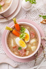 The sour soup (Żurek), polish Easter soup with the addition of sausage, hard boiled egg and vegetables in a ceramic bowl, top view. Traditional Easter dish in Poland