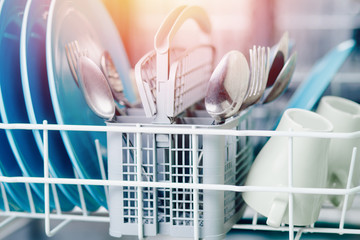 Open dishwasher with clean shine dishes and forks, spoons, cutlery. Concept water saving