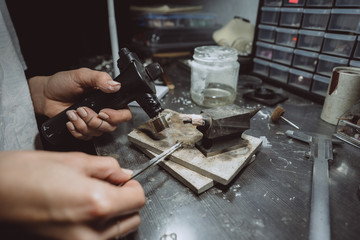 In the workshop, a woman jeweler is busy soldering jewelry