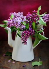 A bouquet of lilacs in an old white coffee pot against a purple background. bright colors of spring. copy space. place for text.