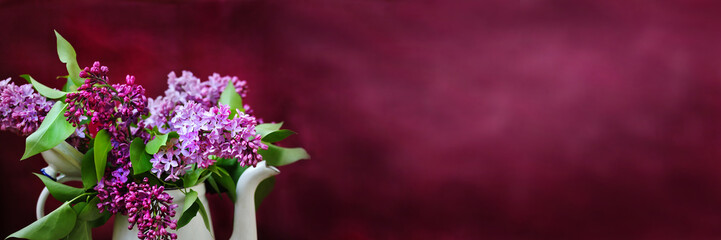 A bouquet of lilacs in an old white coffee pot against a purple background. bright colors of...