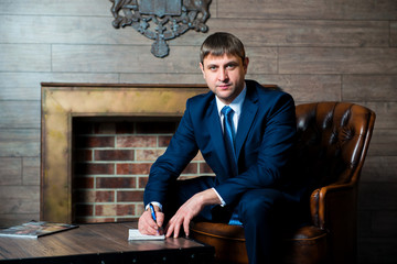 Businessman, lawyer, a man in business suit and tie is sitting at coffee table in office and stating the signature on the documents, make a contract