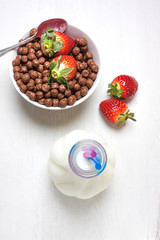 VISTA CENITAL DE DESAYUNO CON FRESAS ROJAS Y CEREALES DE CHOCOLATE Y BOTELLA DE LECHE