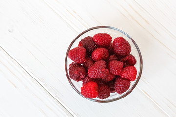 Little glass plate with raspberry on white wooden table. Healthy meal, summer fruits.