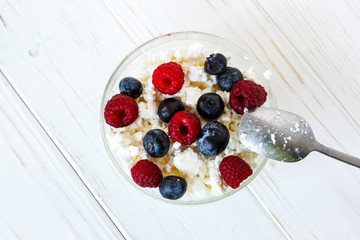 Healthy meal with organic cottage cheese, fresh raspberry, blueberry, peach on white wooden table. close up 