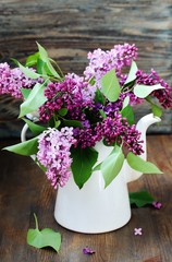 A bouquet of lilacs in an old white coffee pot against a purple background. bright colors of spring. copy space. place for text.