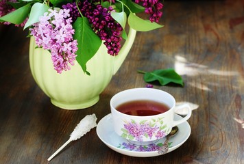 Tea and a bouquet of lilac. Tea in a beautiful cup and a bouquet of lilac in a vase. A spring tea-party. Soft focus