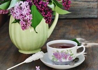 Tea and a bouquet of lilac. Tea in a beautiful cup and a bouquet of lilac in a vase. A spring tea-party. Soft focus