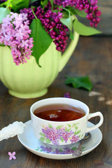 Tea and a bouquet of lilac. Tea in a beautiful cup and a bouquet of lilac in a vase. A spring tea-party. Soft focus