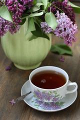 Fototapeta na wymiar Tea and a bouquet of lilac. Tea in a beautiful cup and a bouquet of lilac in a vase. A spring tea-party. Soft focus