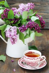 Tea and a bouquet of lilac. Tea in a beautiful cup and a bouquet of lilac in a vase. A spring tea-party. Soft focus