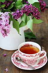 Tea and a bouquet of lilac. Tea in a beautiful cup and a bouquet of lilac in a vase. A spring tea-party. Soft focus