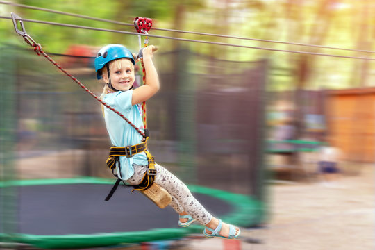 Cute little funny caucasion blond girl in helmet having fun riding rope zipline in adventure park. Children outdoor extreme sport activities concept