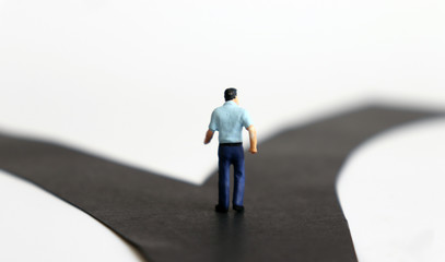 The back of a miniature man standing in front of two fork road.