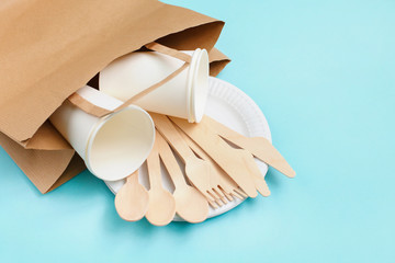 Eco-friendly disposable utensils made of bamboo wood in paper bag on blue background.