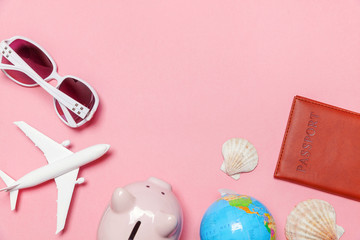 Vacation travel summer weekend sea adventure trip concept. Minimal simple flat lay with plane passport sunglasses globe piggy bank and shell on pink pastel trendy modern background
