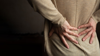 Long working hours and health. Young girl with back pain. Woman with back pain on dark background