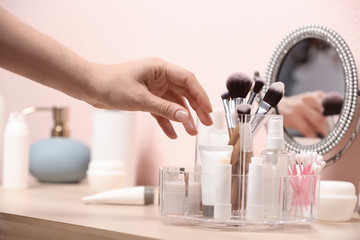 Woman taking cosmetic products from holder on dressing table, closeup