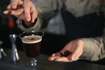 Barman adding coffee bean to martini espresso cocktail at counter, closeup. Space for text
