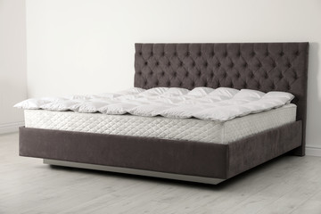 Comfortable bed with new mattress near wall in room. Healthy sleep