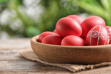 Wooden bowl with red painted Easter eggs on table against blurred background, space for text