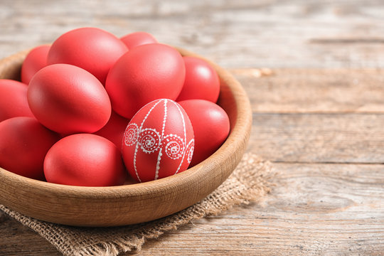 Wooden bowl with red painted Easter eggs on table, space for text