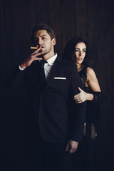 Elegant man in a black suit. Couple at home. Hot woman in a black underwear. Male with cigar