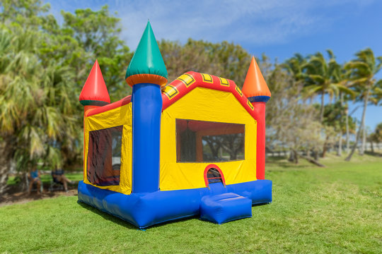 A multi-color castle bounce house photographed from the left side. The inflated bounce house has pops of color everywhere sits at the park on a beautiful sunny day.