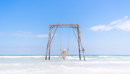 Beautiful Young Blonde Traveler Girl in a white swim suit Swinging on a Sea Swing Framed in the center in Phu Quoc Island, Vietnam.