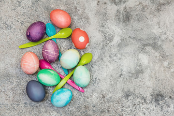 Flatlay für Ostern, bunt gefärbte Ostereier und Eierlöffel auf grauem Tisch