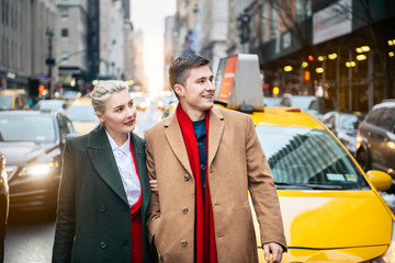 Happy young adult couple walking out from yellow taxi in New York City street and looking to the...