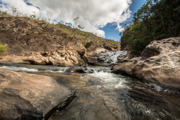 Stony creek in rural Brazil, with lush vegetation around it, on a bright sunny day.
