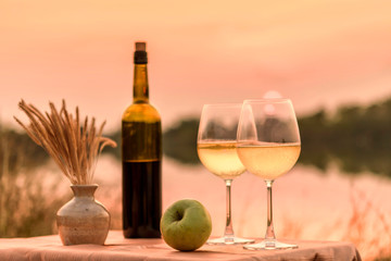 A romantic dinner in summer on a beach at sunset with two glasses of white wine