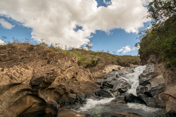 Stony creek in rural Brazil, with lush vegetation around it, on a bright sunny day.