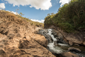 Fototapeta na wymiar Stony creek in rural Brazil, with lush vegetation around it, on a bright sunny day.
