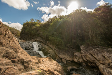 Stony creek in rural Brazil, with lush vegetation around it, on a bright sunny day.